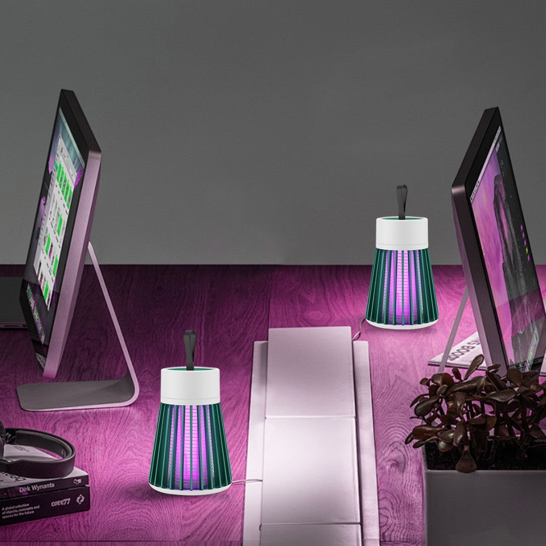 Two computer monitors on a desk with two small lamp-like devices on a purple surface.
